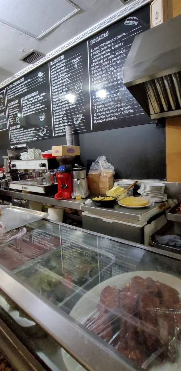 Barra con las pizarras de carta detrás, la cafetera y la vitrina de tapas