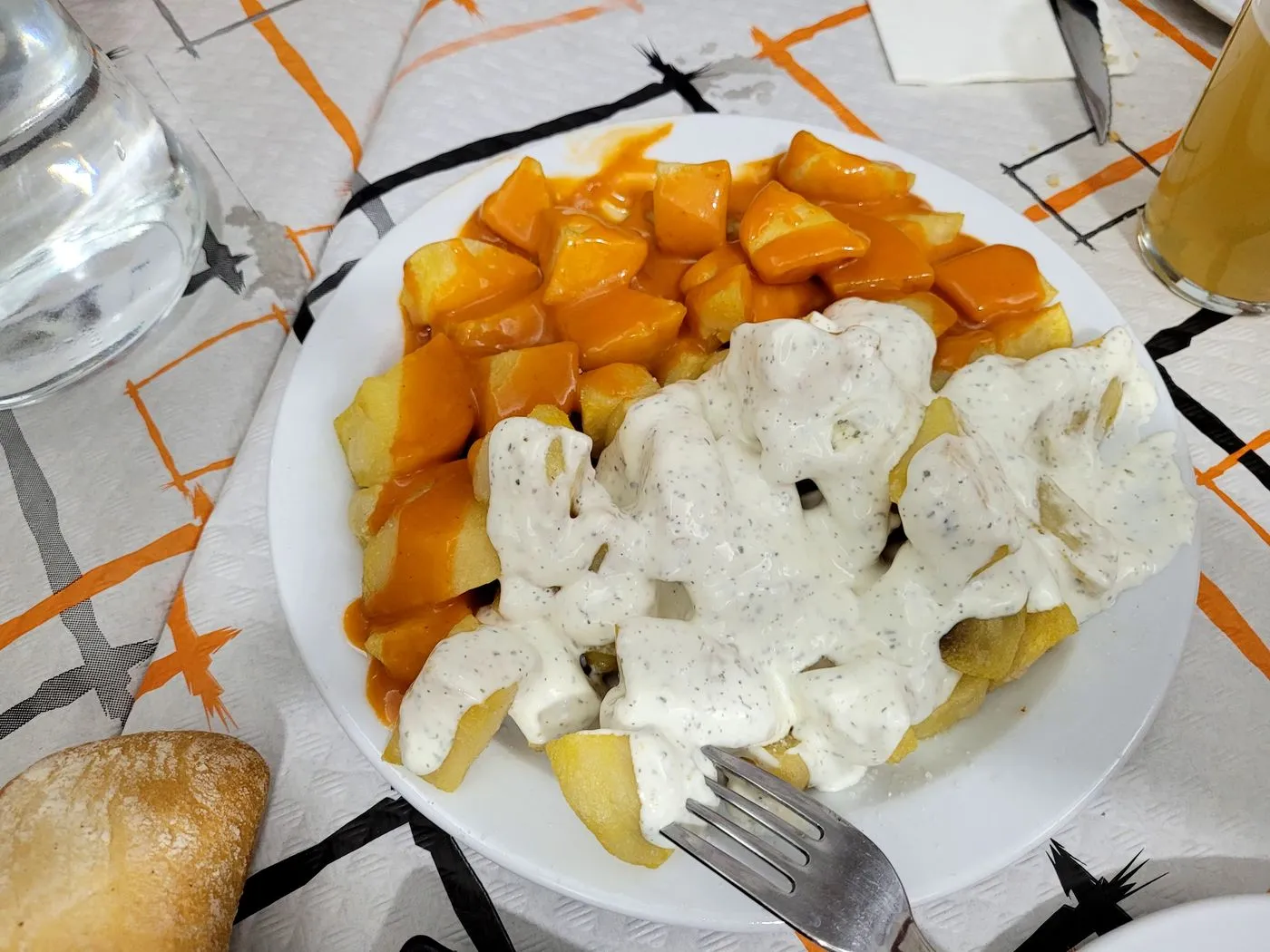 Plato de patatas bravas con salsa brava y alioli sobre un mantel de papel naranja y negro