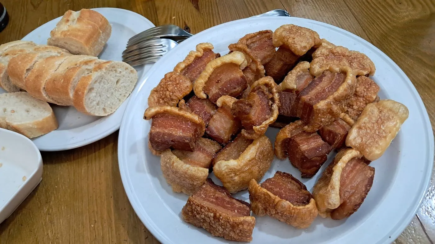Plato de torreznos dorados con pan al lado sobre una mesa de madera