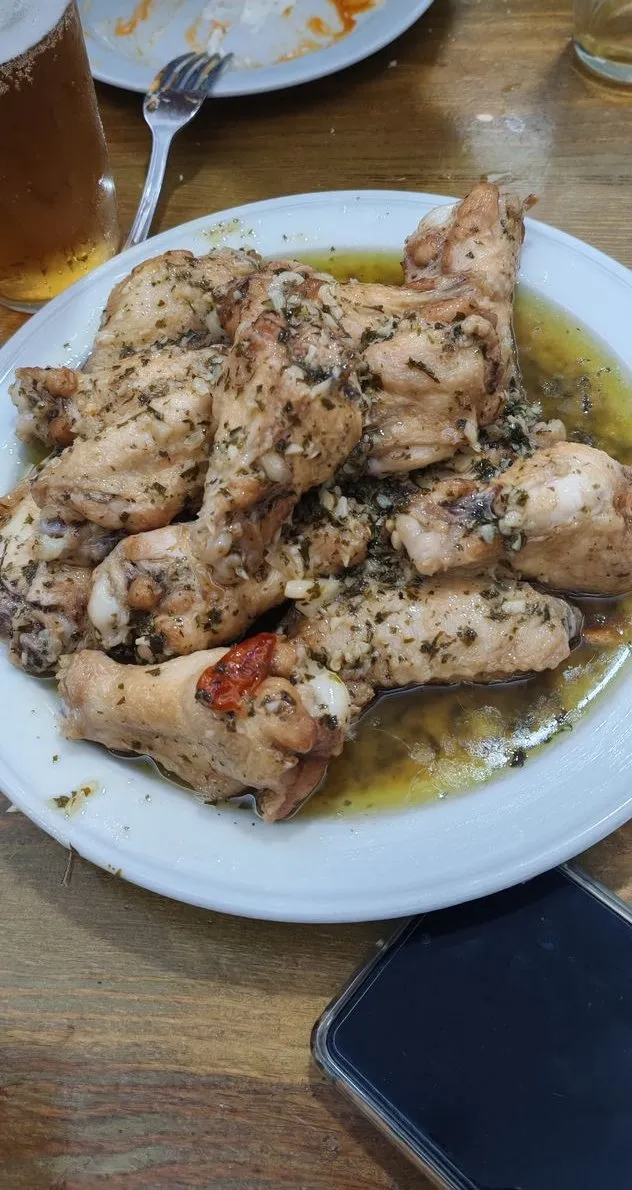 Plato de alitas de pollo con ajo y perejil en aceite, con una caña al lado